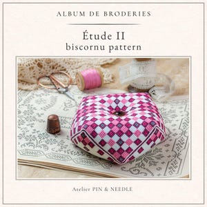 May include: A biscornu pattern in a pink, white, and purple diamond design. The image shows a pincushion, a spool of pink thread, scissors, a thimble, and the text "Album de Broderies Étude II biscornu pattern" and "Atelier PIN & NEEDLE".