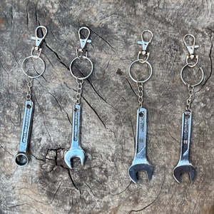 Può includere: Quattro portachiavi a forma di chiave inglese argentati con anelli portachiavi argentati. Le chiavi inglesi sono di dimensioni diverse e hanno il nome del marchio "Wrench" stampato su di esse.