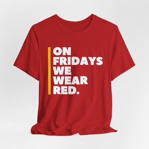 May include: Red t-shirt with a yellow stripe and white text that reads "ON FRIDAYS WE WEAR RED."