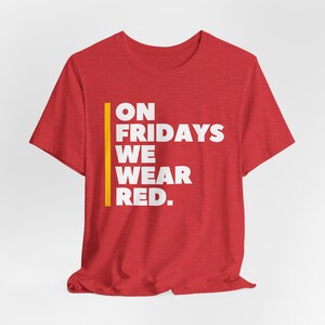May include: Red t-shirt with a white graphic that says "ON FRIDAYS WE WEAR RED."  A yellow vertical line is to the left of the text.
