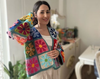 May include: A colorful crocheted cardigan with a floral pattern. The cardigan is made up of squares with different colored flowers. The cardigan is open in the front and has long sleeves.