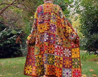 May include: A long, open-front cardigan constructed from numerous square crochet patches, each featuring a multi-colored flower motif. The garment displays a vibrant palette of red, yellow, orange, purple, and green, finished with a solid brown border.