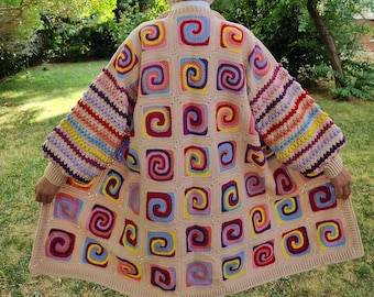 Könnte beinhalten: Ein langer, beiger Häkelcardigan mit bunten Spiralmustern und Streifen an den Ärmeln. Der Cardigan ist aus verschiedenen Farben gefertigt, darunter Rosa, Blau, Gelb und Grün.