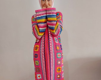 May include: A long pink crochet cardigan with colorful geometric patterns and fringe trim. The cardigan has a zipper closure and is made with a variety of colors, including pink, blue, yellow, green, and orange.