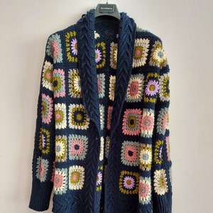 May include: A navy blue crochet cardigan with a long, open front and fringe trim. The cardigan features a colorful geometric pattern with squares of pink, green, yellow, and purple.