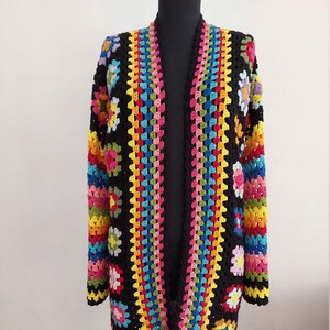 May include: A long, black crochet cardigan with a colorful granny square pattern. The cardigan has a wide, open front and long sleeves.