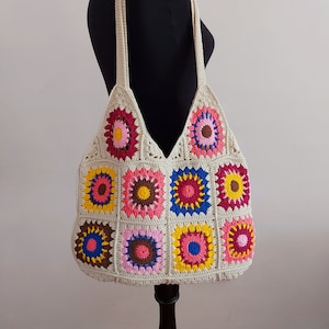 May include: A crocheted tote bag with a patchwork design of colorful granny squares. The bag has a cream base with bright pink, red, yellow, blue, and brown accents.