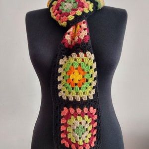 May include: A crocheted scarf with a black background and colorful granny squares in shades of red, orange, yellow, green, and brown.