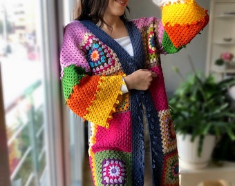 Könnte beinhalten: Eine bunte gehäkelte Strickjacke mit Patchwork-Muster aus Quadraten in den Farben Rosa, Grün, Orange, Gelb und Blau. Die Strickjacke hat einen V-Ausschnitt und lange Ärmel.