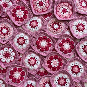 Könnte beinhalten: Eine Sammlung von gehäkelten Quadraten in Rosa, Weiß und Rot mit einem Blumenmuster.