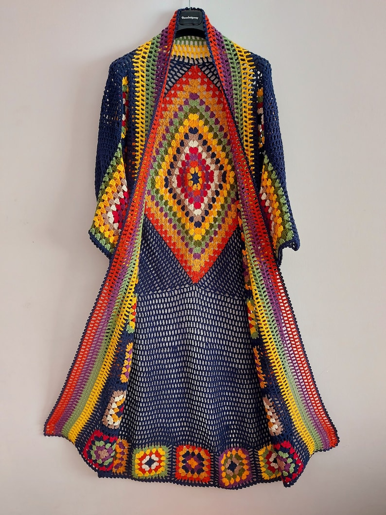 May include: A long, navy blue crochet cardigan with a colorful geometric pattern. The cardigan has a wide, open front and long sleeves.