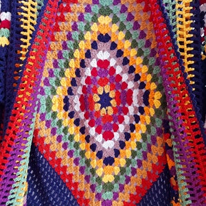 May include: A colorful crocheted shawl with a diamond pattern in shades of red, orange, yellow, green, blue, purple, and white. The shawl is made with a granny square stitch and has a navy blue border.