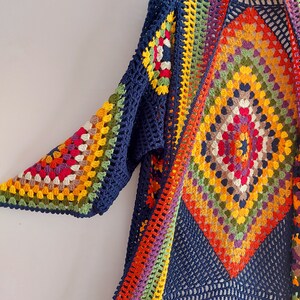 May include: A long, navy blue crochet cardigan with a colorful geometric pattern. The cardigan has a wide, open front and long sleeves.