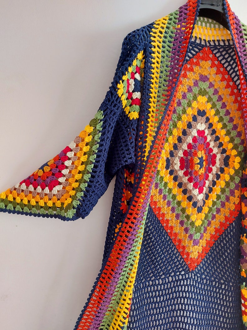 May include: A long, navy blue crochet cardigan with a colorful geometric pattern. The cardigan has a wide, open front and long sleeves.