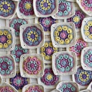 May include: A collection of crocheted squares in various shades of pink, yellow, blue, and green. Each square features a floral design in the centre.