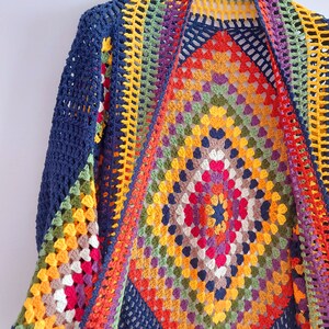 May include: A colorful crochet cardigan with a large granny square pattern in the center. The cardigan is made with a variety of colors, including red, orange, yellow, green, blue, and purple. The cardigan is open in the front and has a wide, flowing shape.