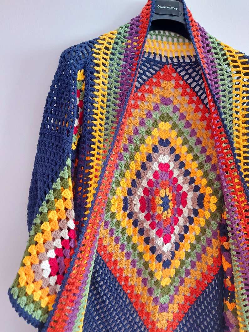 May include: A colorful crochet cardigan with a large granny square pattern in the center. The cardigan is made with a variety of colors, including red, orange, yellow, green, blue, and purple. The cardigan is open in the front and has a wide, flowing shape.