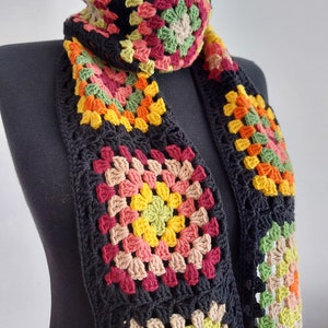 May include: A black crocheted scarf with colorful granny squares. The squares feature shades of red, orange, yellow, green, and brown.