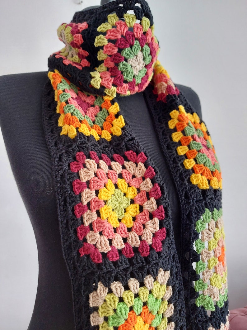 May include: A black crocheted scarf with colorful granny squares. The squares feature shades of red, orange, yellow, green, and brown.