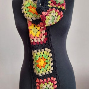 May include: A long, black crocheted scarf with colorful granny squares. The squares are made in shades of red, green, yellow, and brown.