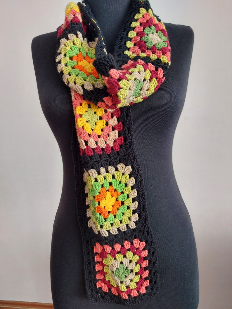 May include: A long, black crocheted scarf with colorful granny squares. The squares are made in shades of red, green, yellow, and brown.