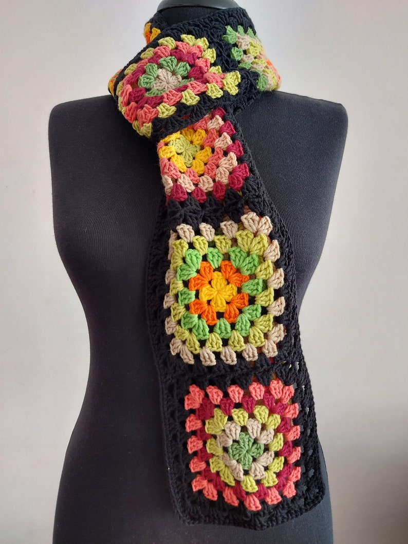 May include: A crocheted scarf with a black background and colorful granny squares in shades of red, orange, yellow, green, and brown.