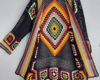 Puede incluir: Una chaqueta de punto de ganchillo negra con un patrón geométrico colorido. La chaqueta tiene una abertura larga en la parte delantera y mangas tres cuartos.