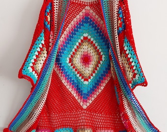 May include: A red crochet cardigan with a colorful geometric pattern. The cardigan has a loose fit and a long, flowing style. It features a crocheted border with pom-poms.