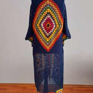 May include: A long, navy blue crochet cardigan with a colorful diamond-shaped pattern on the back. The cardigan has a loose fit and a wide, open neckline.