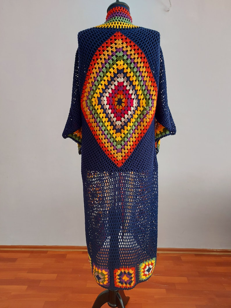 May include: A long, navy blue crochet cardigan with a colorful diamond-shaped pattern on the back. The cardigan has a loose fit and a wide, open neckline.