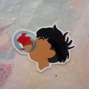 May include: A sticker of a cartoon character blowing a bubble with a red fish inside. The character has black hair and is wearing a white shirt.