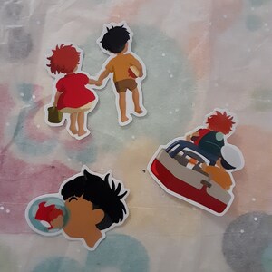 May include: Four colorful stickers featuring characters from the animated film 'Ponyo'. The stickers are on a white background. The stickers feature a girl with red hair, a boy with brown hair, a boy with brown hair and a red fish, and a boy with brown hair and a red boat.