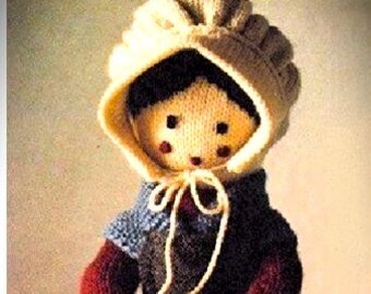 May include: A knitted doll featuring a cream-colored bonnet with ties, black hair, and rosy cheeks. The doll wears a dark blue apron over a maroon long-sleeved top, a matching maroon skirt, white ruffled undergarments, and black boots.
