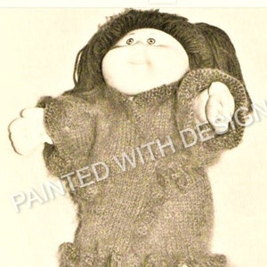 Könnte beinhalten: Eine Strickpuppe mit braunen Haaren und einem braunen Kleid. Die Puppe trägt braune Strickschuhe.