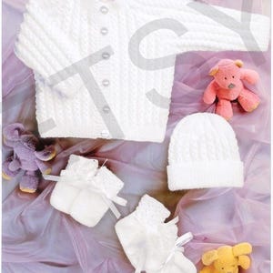 Puede incluir: Un cárdigan de punto blanco para bebé con botones frontales, un gorro de punto blanco a juego y dos patucos de punto blanco con lazos. El conjunto se acompaña de tres pequeños peluches en colores rosa, morado y amarillo.