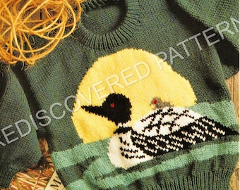 May include: A dark green knitted sweater featuring a large yellow circular moon graphic behind a black and white loon swimming on water. The loon has a small chick on its back. The sweater has a ribbed crew neckline, cuffs, and hem.