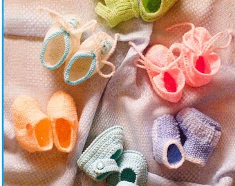 May include: A collection of six pairs of handmade knitted baby booties in various colors including lime green, white with blue trim, soft pink, peach, light blue with buttons, and lavender, all arranged on a textured fabric surface.