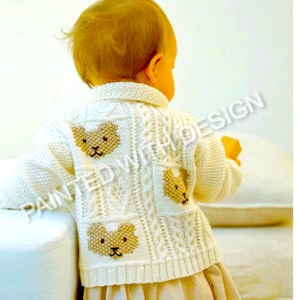 May include: A white knitted cardigan with a cable knit pattern and brown bear appliques on the back. The cardigan is being worn by a child.
