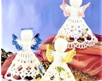 May include: Three crocheted angel figurines featuring white dresses with intricate lace patterns. Each angel has a distinct halo and wing color: one with blue, one with yellow, and one with pink. Small fabric flowers are attached to each dress.