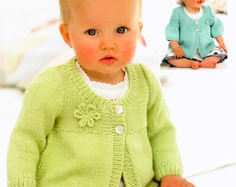 May include: A light green knit cardigan featuring a round neckline, long sleeves, and a small crocheted flower detail on the chest. The garment is fastened with two white buttons at the front and has a ribbed texture along the cuffs and hem.