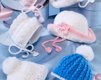 May include: A collection of six crocheted hats and bonnets in white, pink, and blue. The set includes two white brimmed hats with floral accents, two white bonnets, one pink and white bonnet, and one blue and white hat with a white pom-pom.