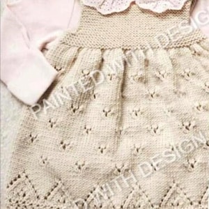 May include: A light beige knitted dress with a decorative pattern. The dress has a round, lace-trimmed collar and long sleeves. The dress is a soft, neutral color, suitable for a baby or toddler.