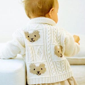 May include: A cream-coloured knit cardigan featuring a textured cable knit pattern and three distinct beige bear face motifs on the back. The garment has a collared neckline, long sleeves, and a ribbed hem, worn over a plain light-coloured skirt.