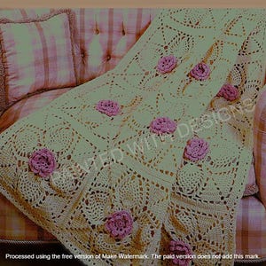 May include: A cream-coloured, crocheted blanket featuring a floral design and pink rose accents. The blanket is draped over a pink upholstered armchair with a matching cushion. The intricate pattern and soft colours of the blanket create a cosy, handmade aesthetic.