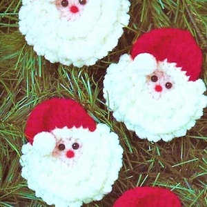 May include: Four round, crocheted Santa Claus ornaments featuring bright red hats with white pom-poms, white textured beards, pink faces, small black eyes, and red noses. Each ornament is crafted with yarn to create a soft, circular appearance.