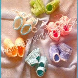 以下が含まれることがあります： ピンク、ブルー、グリーン、イエローなど、さまざまな色の8つの手編みのベビーブーティのセット。ブーティは白い手編みの毛布の上に置かれています。