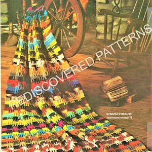 Peut inclure: Une couverture en crochet colorée avec une bordure en franges, présentant une variété de couleurs, notamment le rouge, le jaune, le bleu, le vert et le noir. La couverture est drapée sur une roue à filer et un fauteuil à bascule dans un cadre rustique. Le texte "Scraps of Beauty" et "Instructions on page 12" est visible dans le coin inférieur droit de l'image.