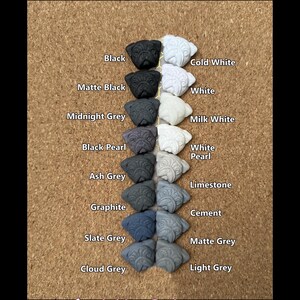 May include: A display of pug-shaped decorative items in various colors, including black, white, and several shades of gray. The image includes text indicating the available colors and a disclaimer about design availability.