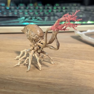 Puede incluir: Figura detallada de criatura de color beige con cabeza bulbosa, múltiples tentáculos y estructura coralina. La figura está sobre una superficie de madera, mostrando su intrincado diseño y textura.