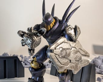 May include: A dark blue and silver action figure of a robot with a weapon in one hand and a shield in the other. The robot has a yellow face and sharp spikes on its back.